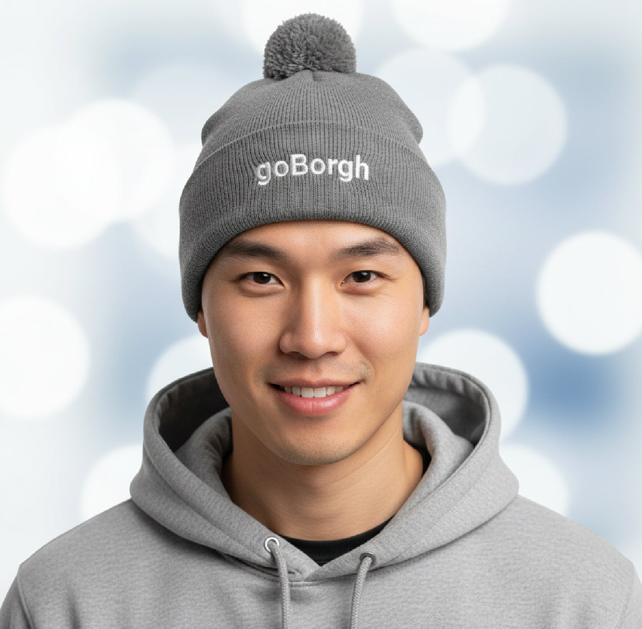 Man wearing a gray goBorgh knit beanie with pom against a winter background