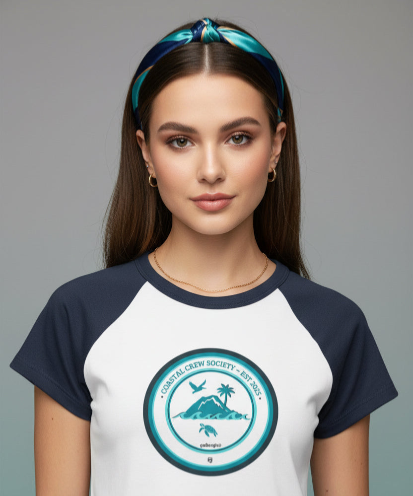 Close-up headshot of a Gen Z model wearing the goBorgh® Island Society Seal cropped baby tee, styled with minimal jewelry and a navy-turquoise silk headband against a neutral background.