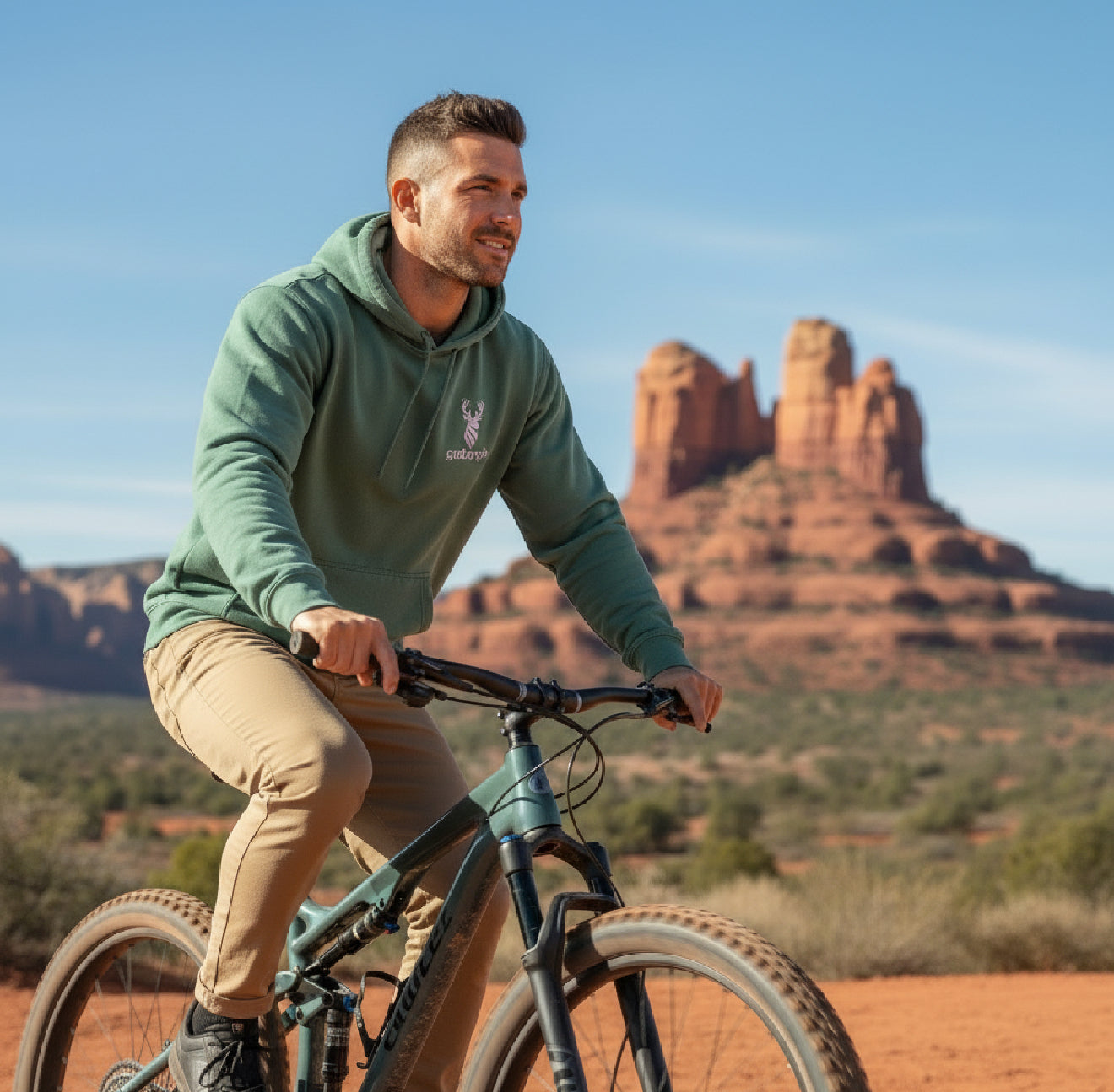 Man biking in desert terrain wearing the goBorgh® Highland Frontier™ Stag hoodie in Pigment Alpine Green
