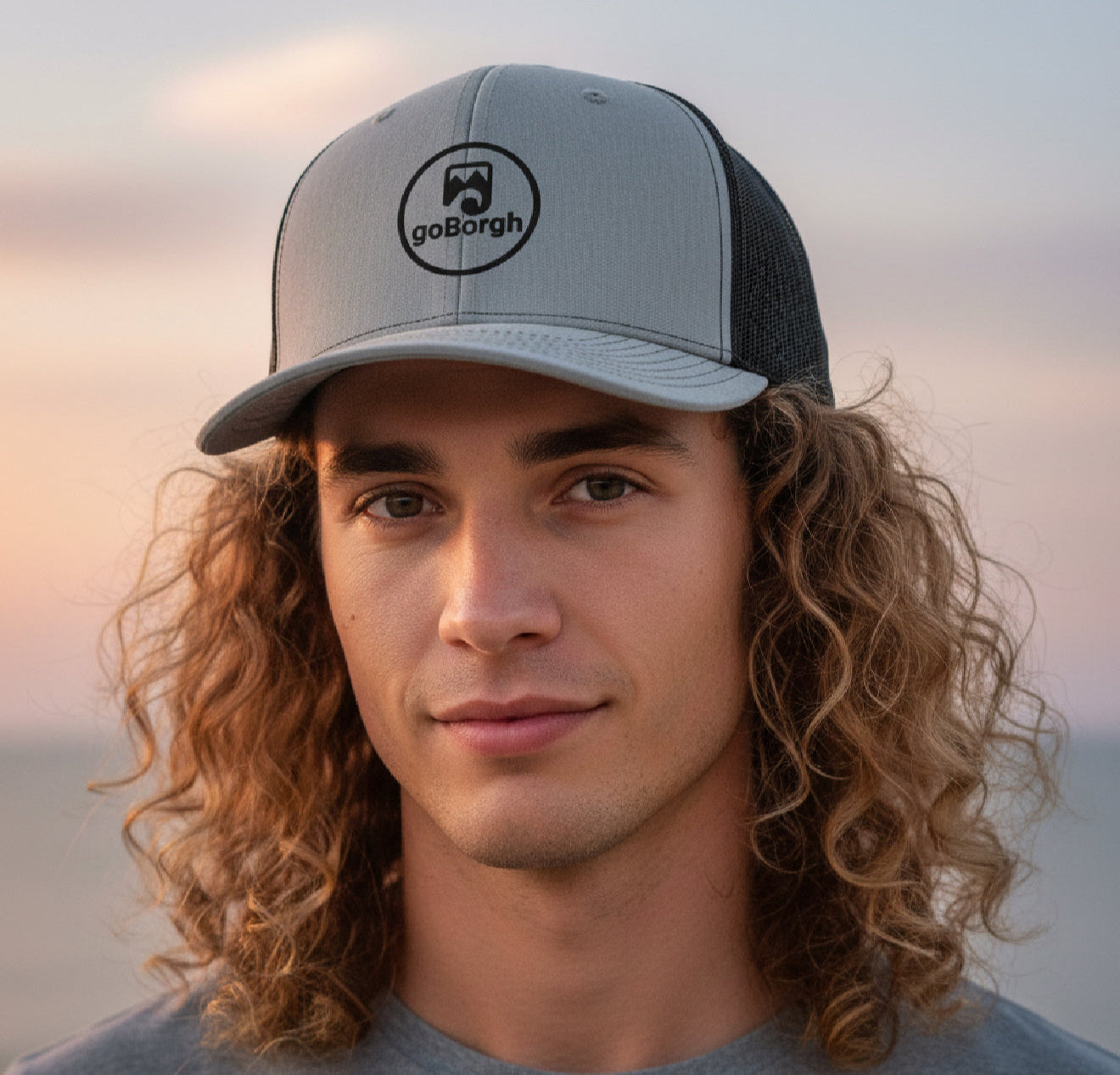 Man with curly hair wearing a goBorgh® Coastal Crew snapback trucker cap outdoors